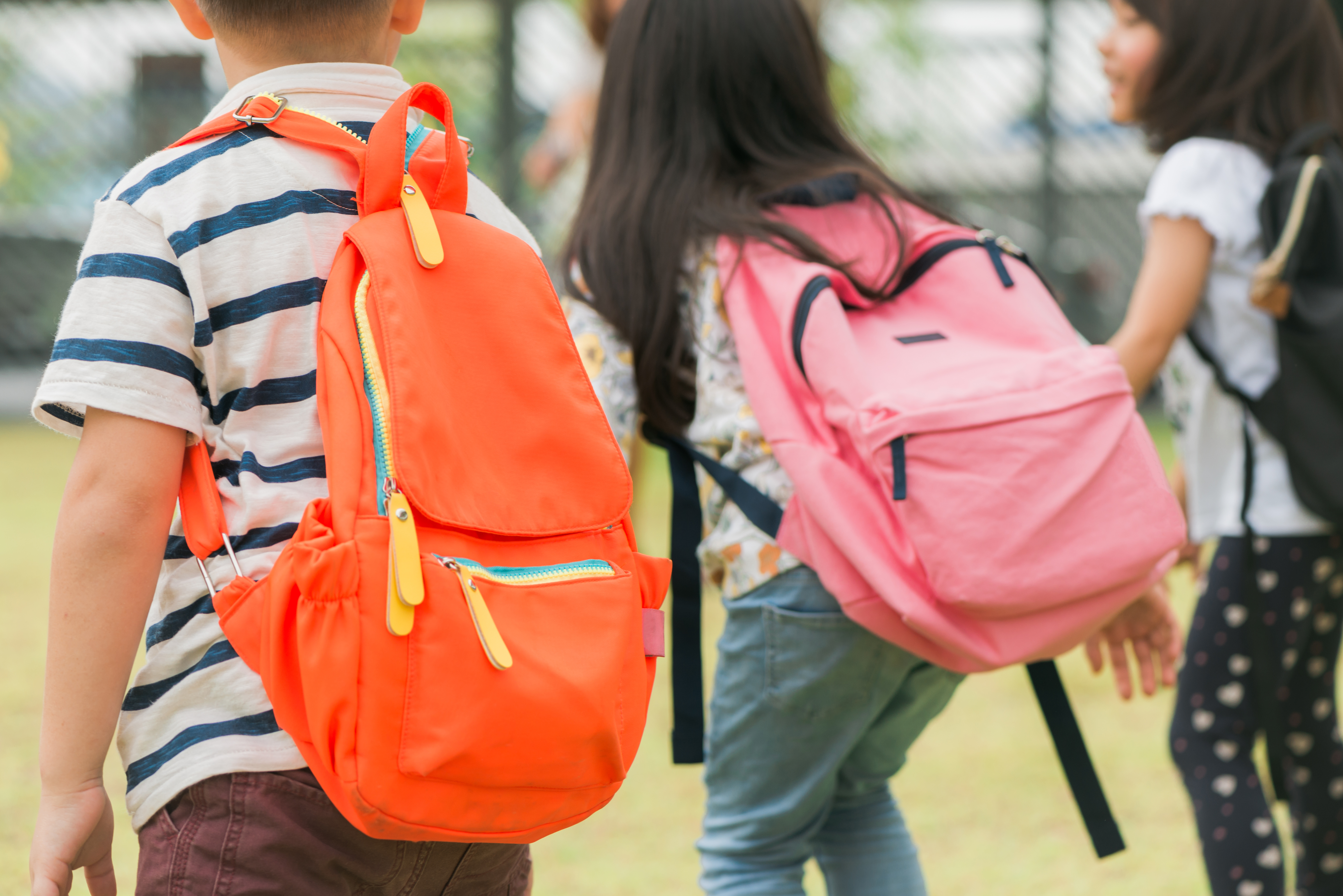 three pupils of primary school go hand in hand boy and girl with school bags behind the back beginning of school lessons warm day of fall back to school little first graders